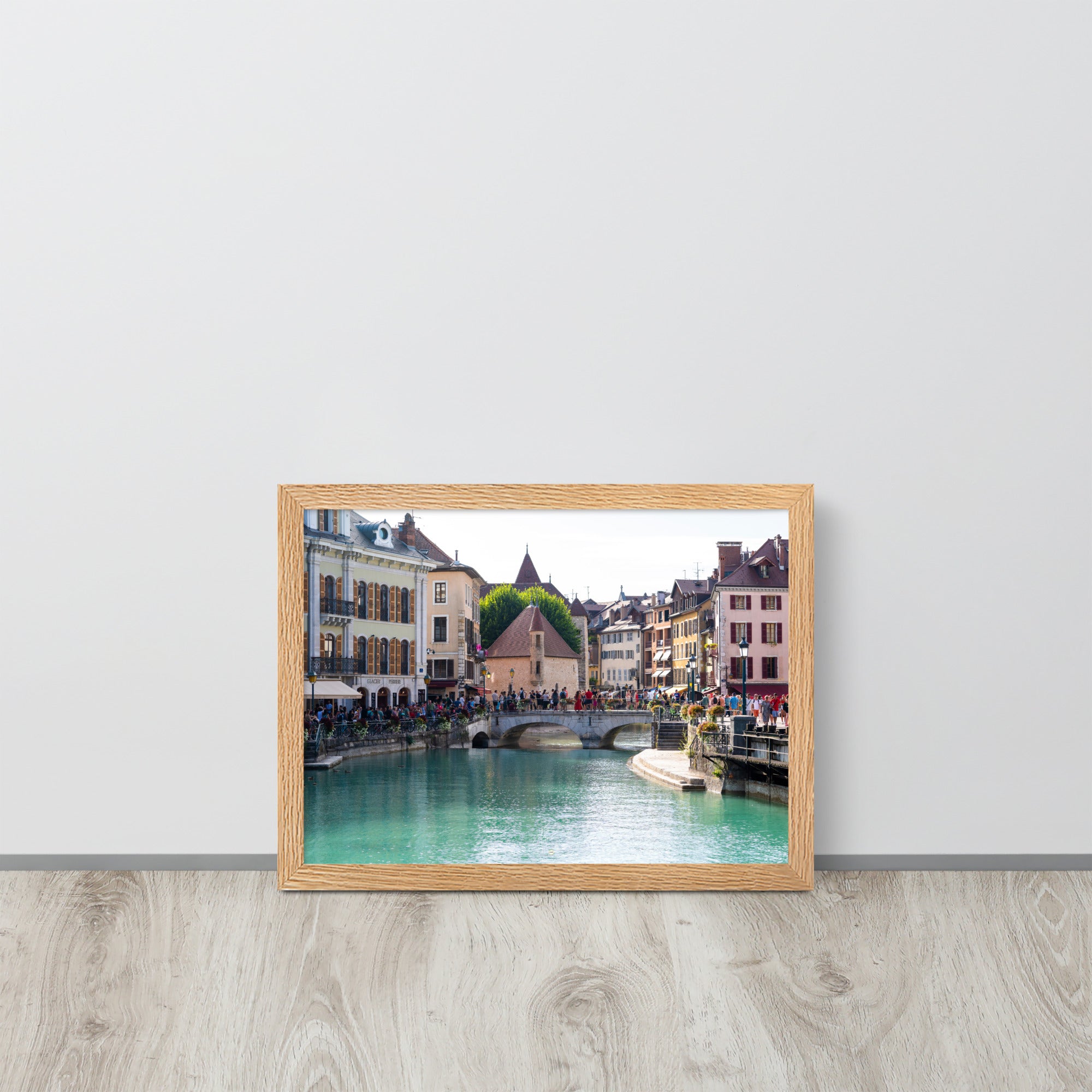 Vue estivale d'Annecy, mettant en lumière le Pont Perrière et le Palais de l'Île, encadrée d'un bois de chêne.