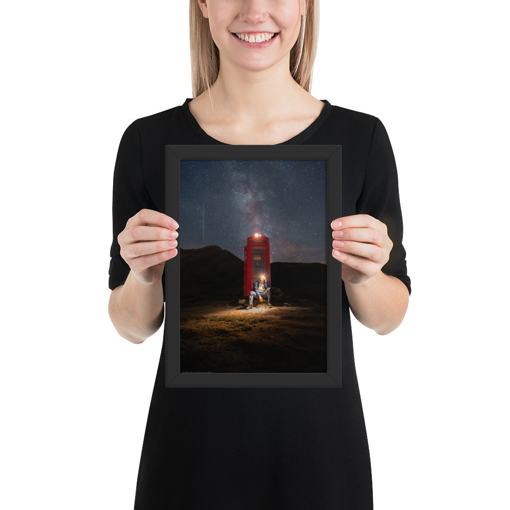 Cabine téléphonique rouge illuminée au milieu de montagnes sombres sous un ciel étoilé par la Voie Lactée, un homme contemple la scène – œuvre signée Brandon Valette.