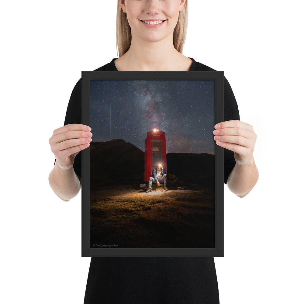 Cabine téléphonique rouge illuminée au milieu de montagnes sombres sous un ciel étoilé par la Voie Lactée, un homme contemple la scène – œuvre signée Brandon Valette.