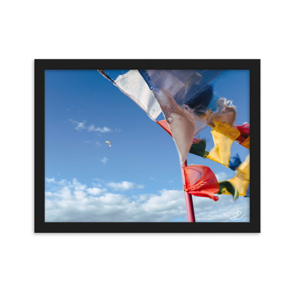 Photographie capturant des drapeaux colorés ondulant au vent et un parapente dans un ciel bleu, par Ilan Shoham, symbolisant la joie et l'esprit d'aventure.