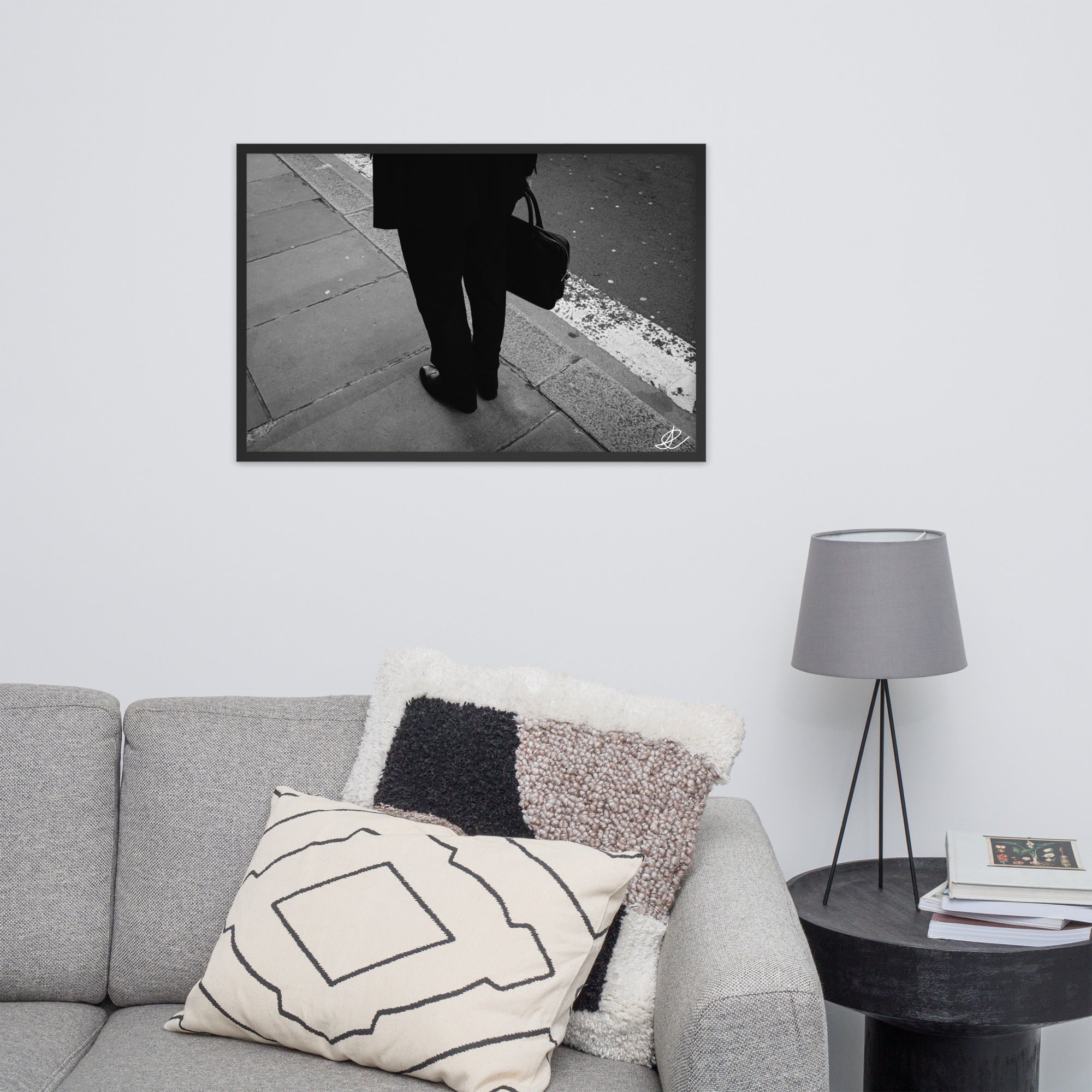 Photographie noir et blanc 'L'Homme d'Affaires' par Ilan Shoham, capturant une scène urbaine quotidienne avec un focus sur une paire de jambes, un sac à documents et un costume noir contre le décor brut du trottoir, encadrée élégamment pour un impact visuel puissant.