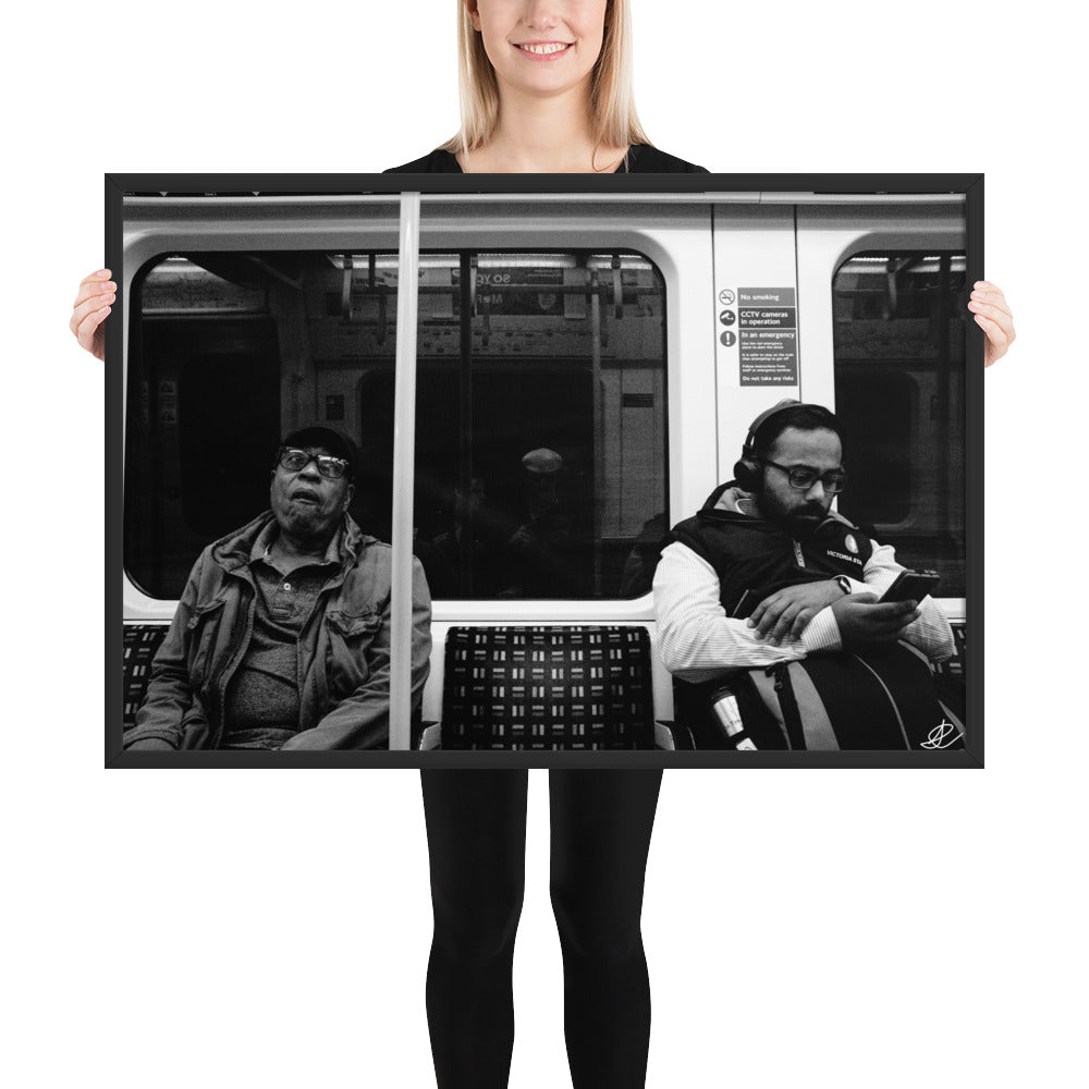 Poster encadré 'Fin de journée' en noir et blanc par Ilan Shoham, capturant une scène paisible du métro londonien avec un siège vide encadré par deux individus assis, symbolisant les distances sociales dans l'agitation urbaine.