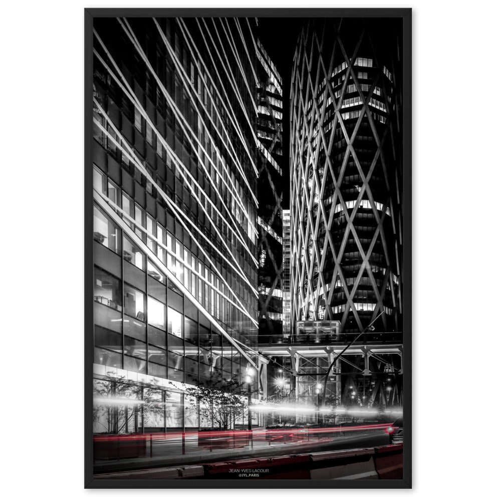 Photographie noir et blanc par Jean-Yves Lacour, montrant le mouvement fluide des lumières des véhicules en contraste avec les bâtiments modernes, capturant l'énergie de la ville.