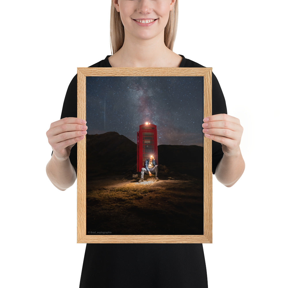 Cabine téléphonique rouge illuminée au milieu de montagnes sombres sous un ciel étoilé par la Voie Lactée, un homme contemple la scène – œuvre signée Brandon Valette.