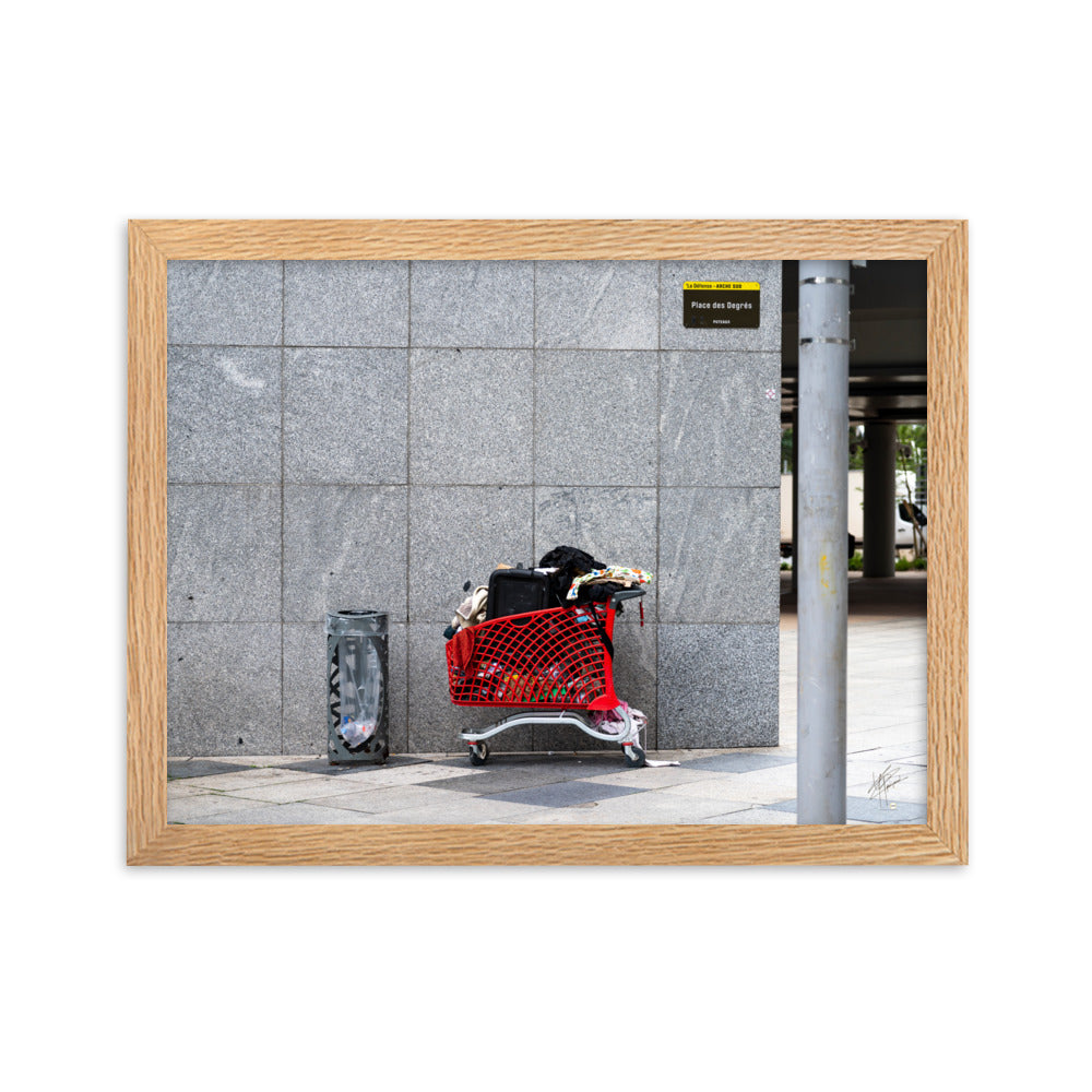 Photographie d'un caddie rouge abandonné à La Défense, juxtaposé à une poubelle, évoquant une méditation sur la consommation et l'abandon dans un contexte urbain moderne.