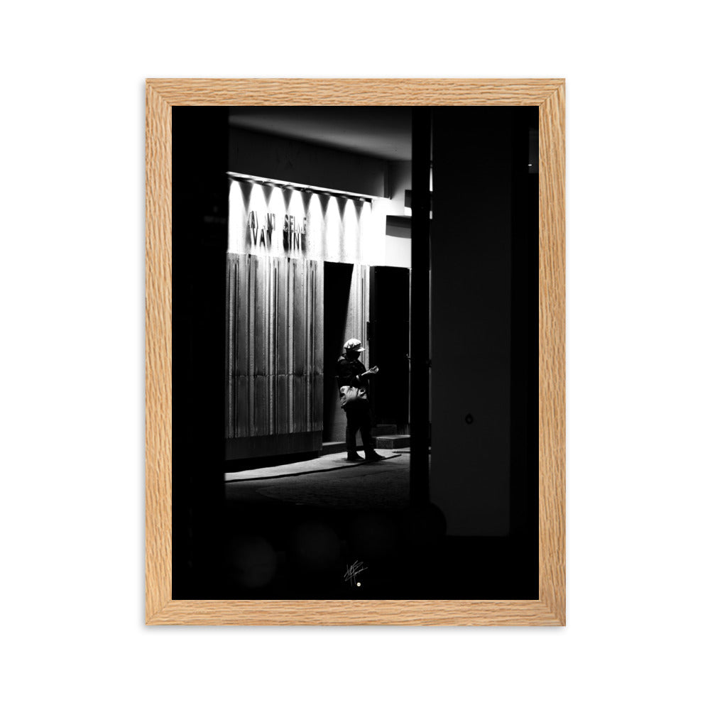 Photographie en noir et blanc d'une femme éclairée par son téléphone dans une rue sombre, mettant en évidence le contraste lumineux de la scène urbaine.