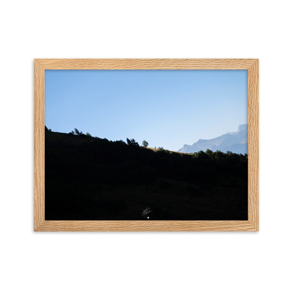 Poster encadré 'Le Tournis', mettant en scène un arbre solitaire éclairé par le soleil sur un flanc de montagne sombre, capturant l'essence du mystère et de la lumière alpine.