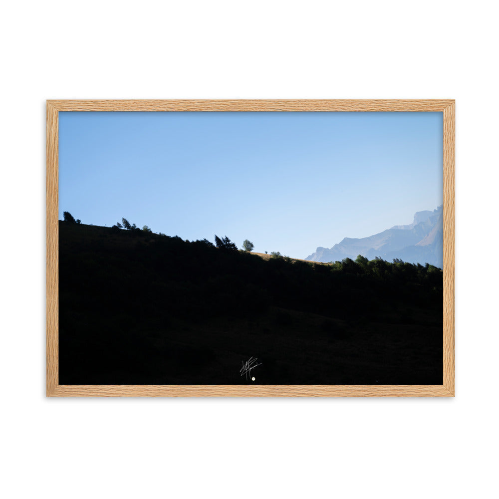 Poster encadré 'Le Tournis', mettant en scène un arbre solitaire éclairé par le soleil sur un flanc de montagne sombre, capturant l'essence du mystère et de la lumière alpine.