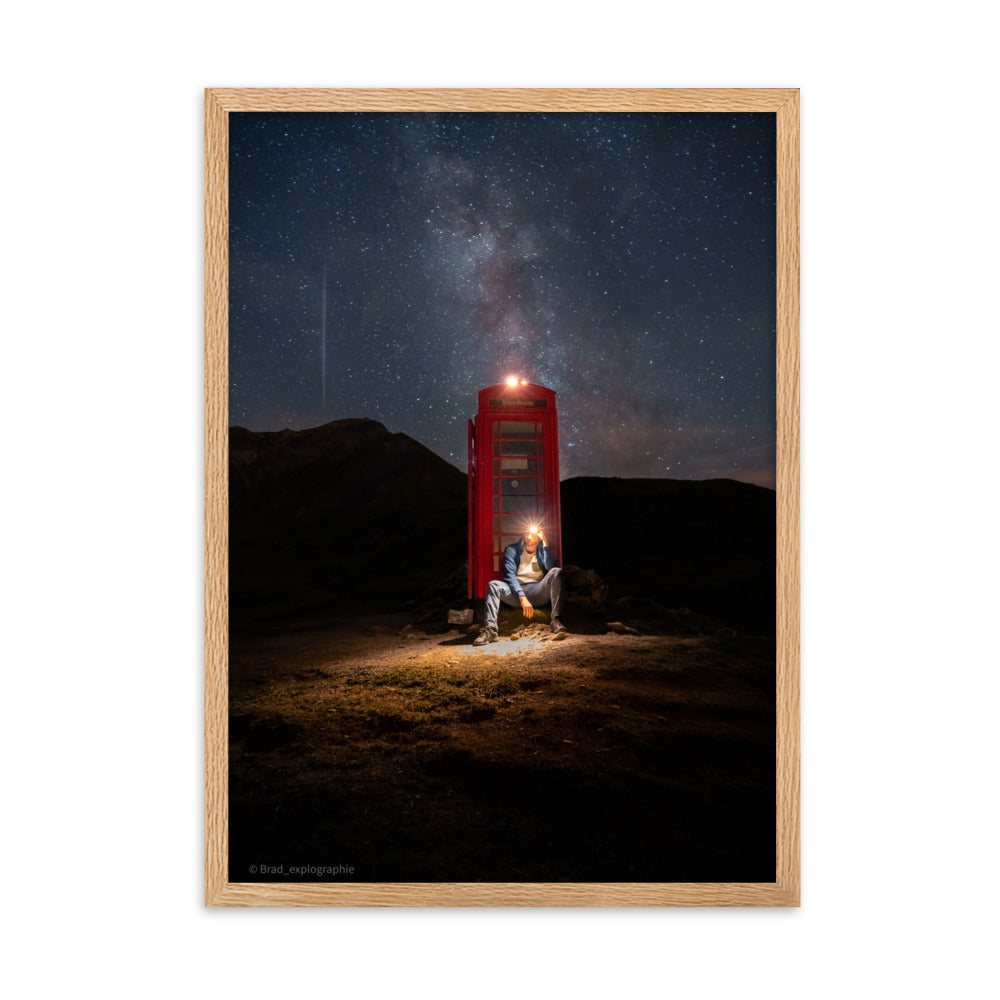 Cabine téléphonique rouge illuminée au milieu de montagnes sombres sous un ciel étoilé par la Voie Lactée, un homme contemple la scène – œuvre signée Brandon Valette.