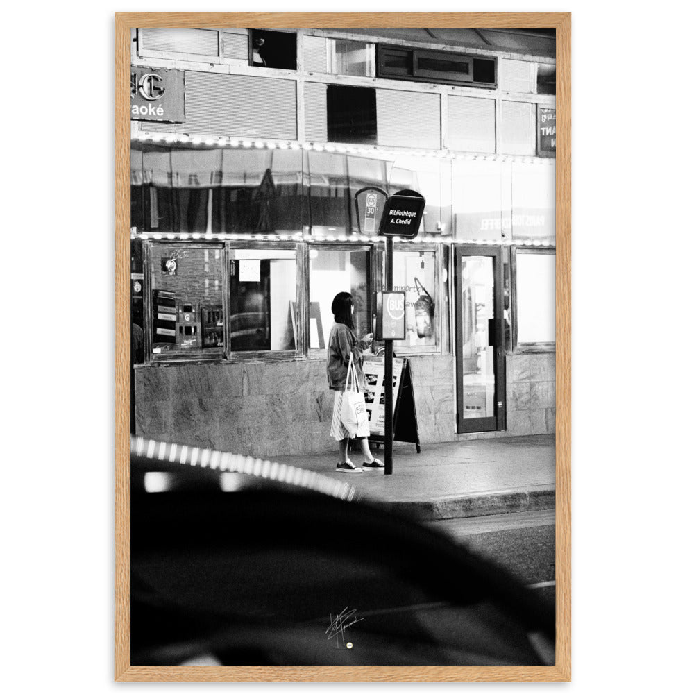 Photographie en noir et blanc d'une femme éclairée par son téléphone dans une rue sombre, mettant en évidence le contraste lumineux de la scène urbaine.