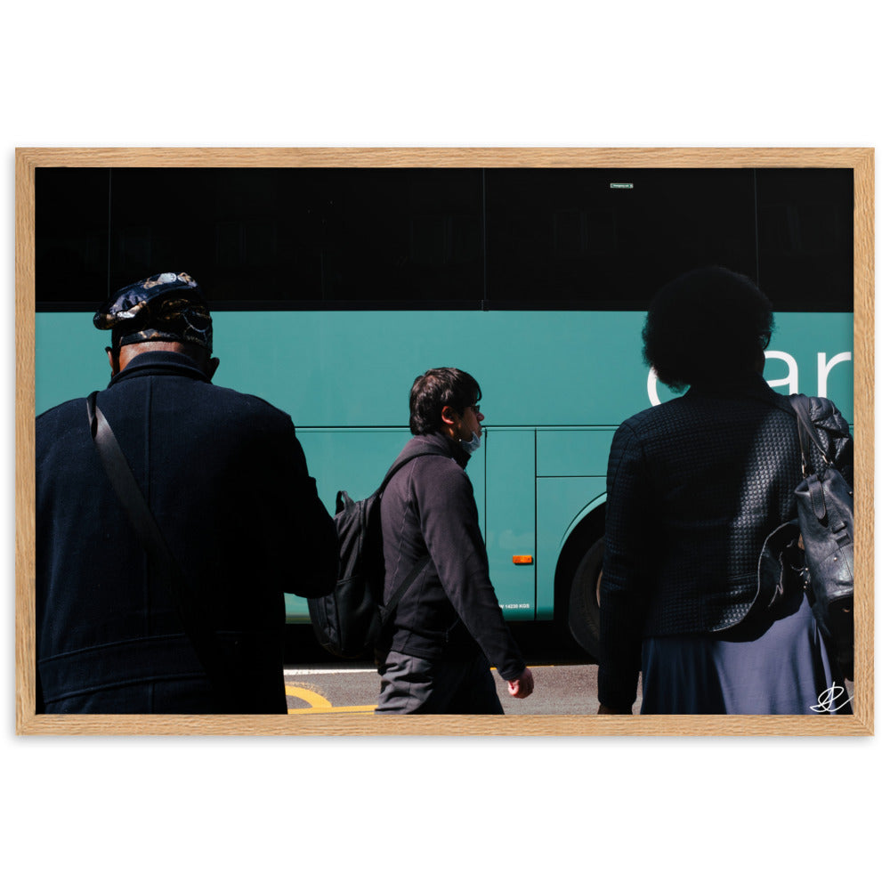 Photographie encadrée 'Arrêt de Bus' par Ilan Shoham, illustrant une scène urbaine londonienne riche en narratif, avec deux individus au premier plan, un passant solitaire au second, et un bus flou en arrière-plan, symbolisant la complexité et la beauté du quotidien.