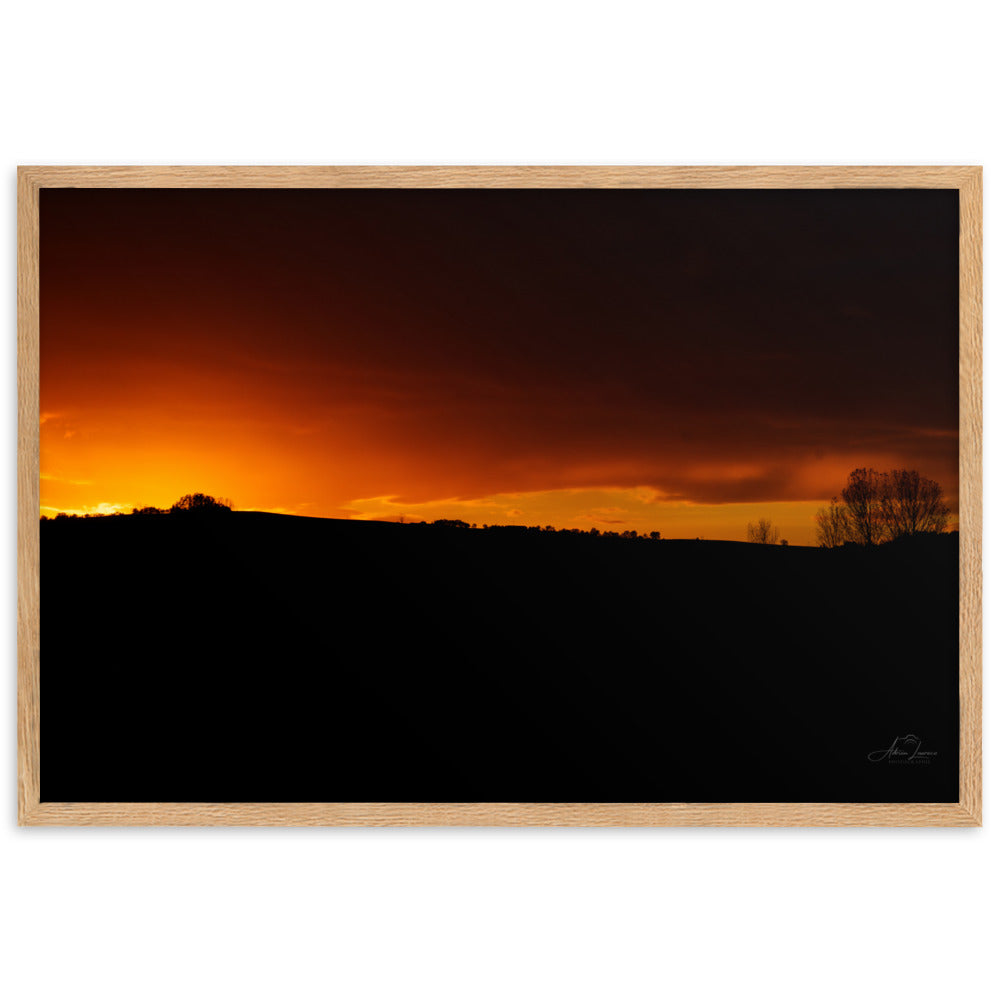 Photographie d'un coucher de soleil flamboyant, par Adrien Louraco, illustrant un ciel vibrant de teintes ardentes contre une silhouette de campagne.