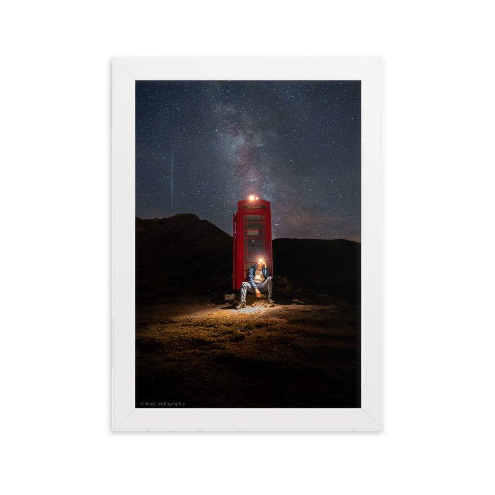 Cabine téléphonique rouge illuminée au milieu de montagnes sombres sous un ciel étoilé par la Voie Lactée, un homme contemple la scène – œuvre signée Brandon Valette.