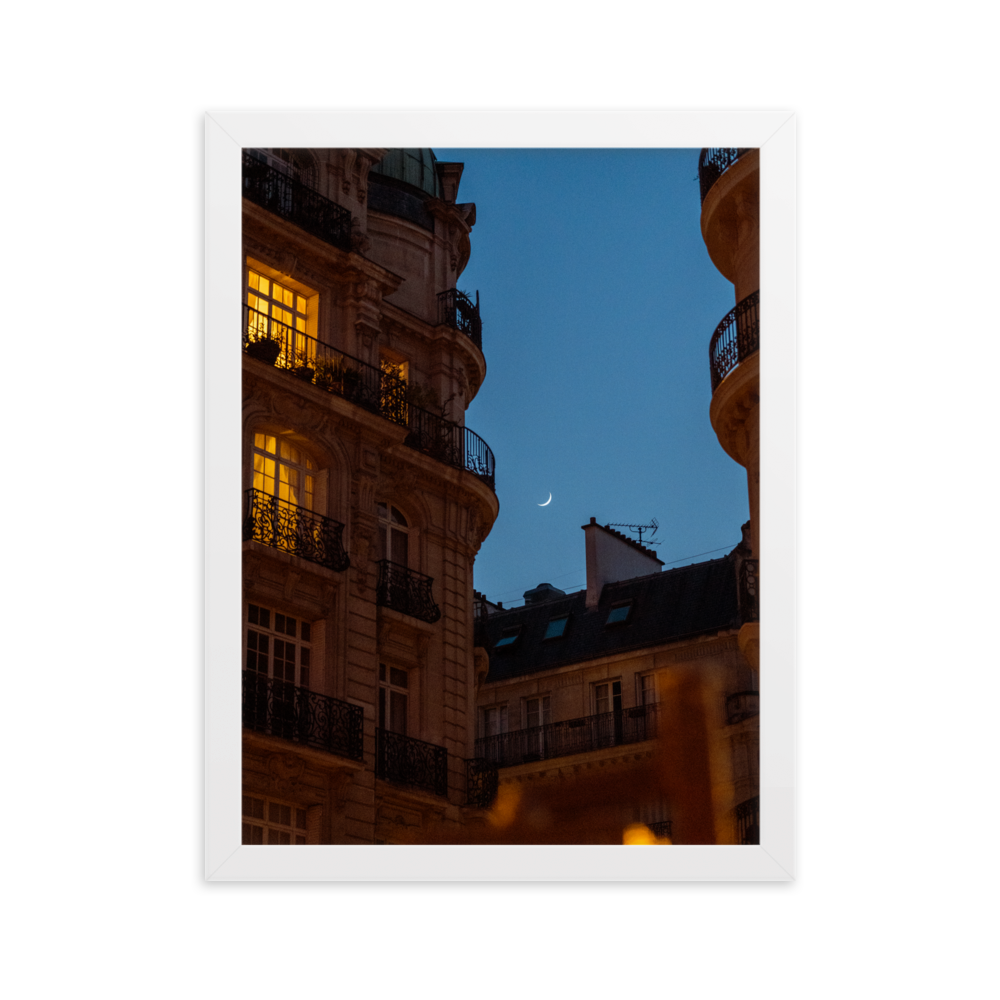 Croissant de lune entre des immeubles haussmanniens éclairés la nuit.