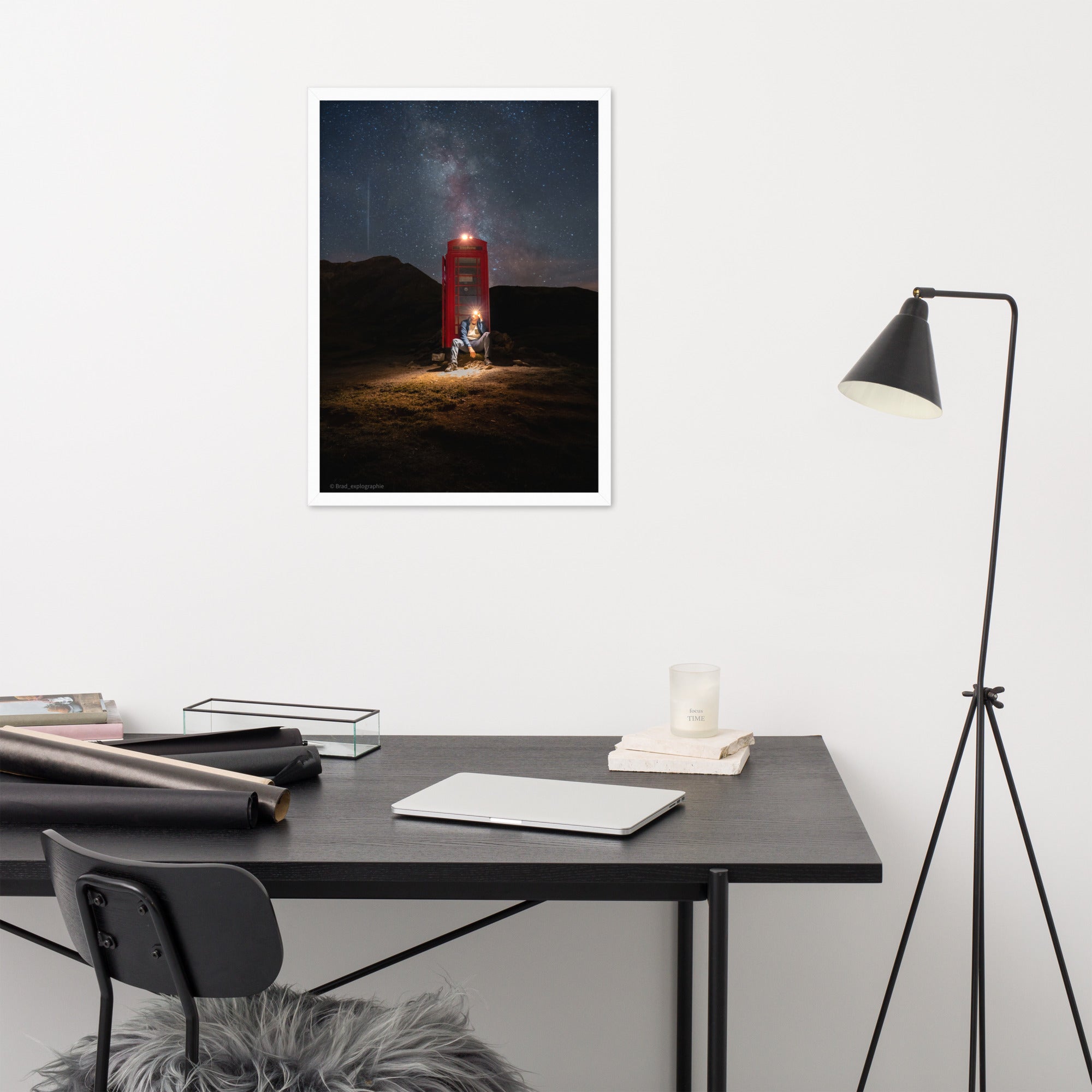 Cabine téléphonique rouge illuminée au milieu de montagnes sombres sous un ciel étoilé par la Voie Lactée, un homme contemple la scène – œuvre signée Brandon Valette.