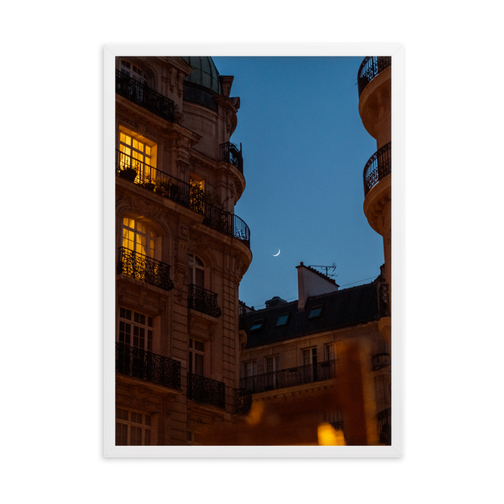 Croissant de lune entre des immeubles haussmanniens éclairés la nuit.