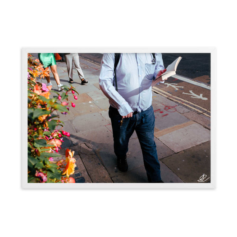 Photographie 'La Marche' par Ilan Shoham, représentant un homme en chemise bleue marchant paisiblement et lisant un livre dans les rues animées de Londres, symbolisant la sérénité et la résistance au milieu du tumulte urbain, tout en apportant une tranquillité visuelle à votre espace de vie ou de travail.