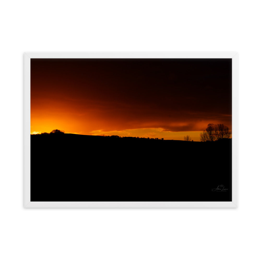 Photographie d'un coucher de soleil flamboyant, par Adrien Louraco, illustrant un ciel vibrant de teintes ardentes contre une silhouette de campagne.