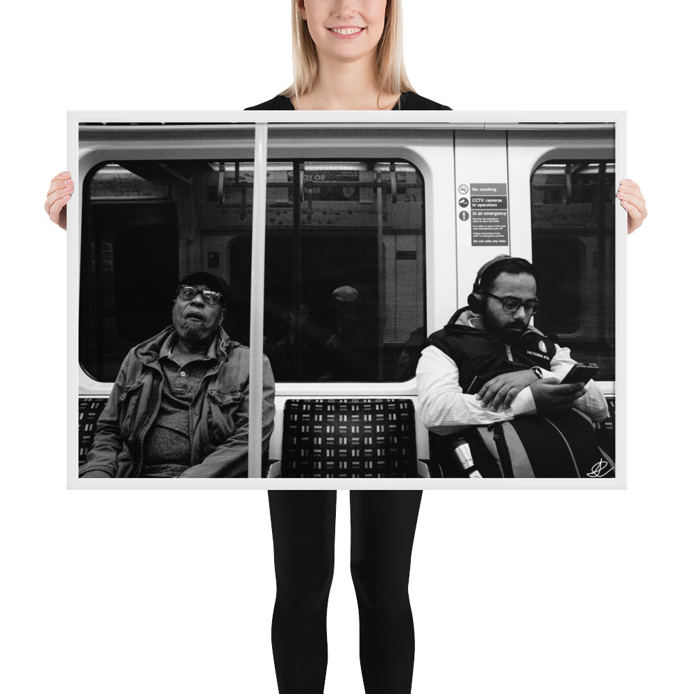 Poster encadré 'Fin de journée' en noir et blanc par Ilan Shoham, capturant une scène paisible du métro londonien avec un siège vide encadré par deux individus assis, symbolisant les distances sociales dans l'agitation urbaine.