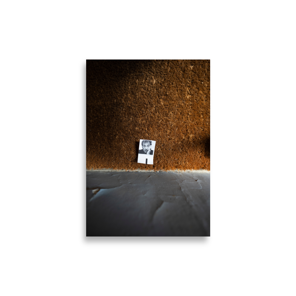 Poster d'une photographie représentant une petite photo posée sur un tapis à l'entrée d'un immeuble parisien.