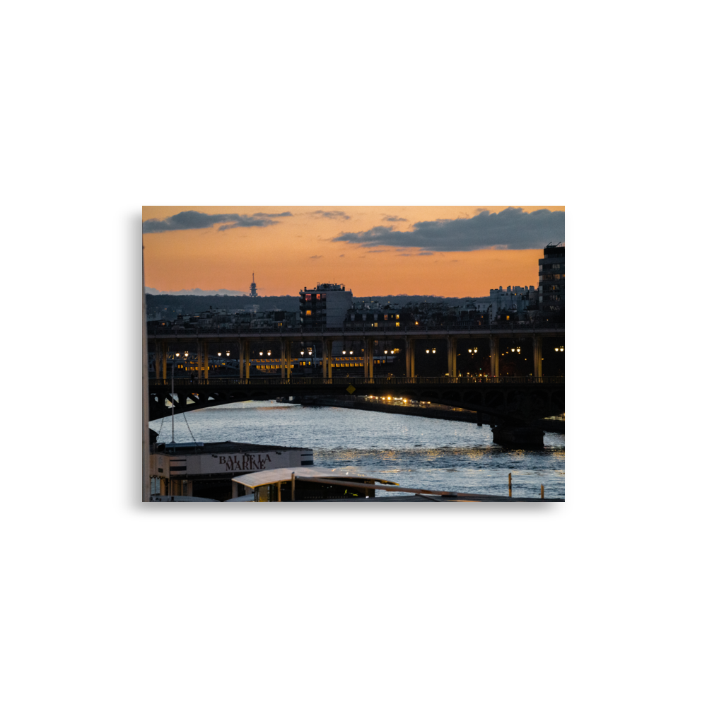 Photographie nocturne du Pont de Bir-Hakeim à Paris, avec des bateaux amarrés aux quais de la Seine et le RER en arrière-plan, sous un ciel teinté d'orange.