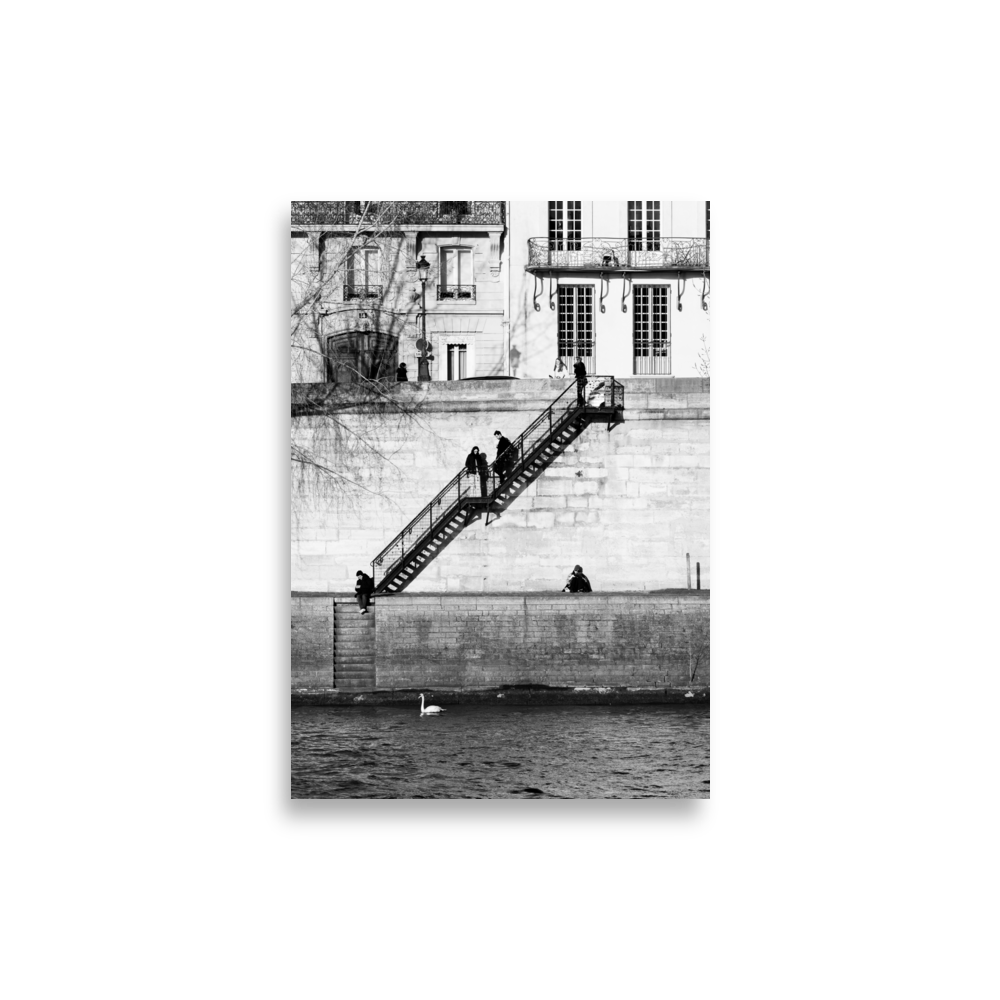 Photographie noir et blanc de personnes installées tranquillement sur les quais à Paris, encadrées par deux escaliers symétriques.