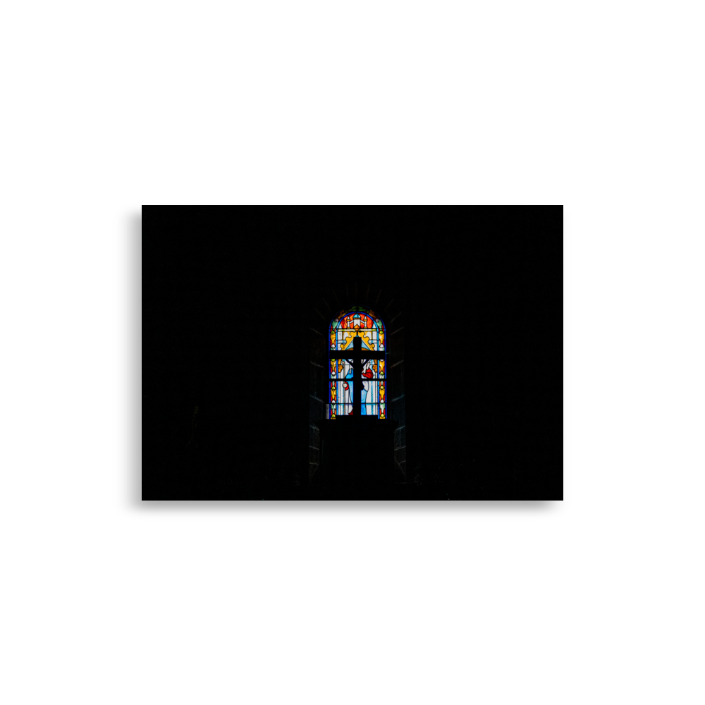 Photographie d'une croix avec Jésus dans une église, éclairée par un vitrail en arrière-plan.