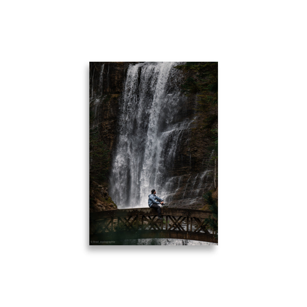 Homme méditatif assis sur une structure en bois au-dessus d'une rivière tumultueuse avec une cascade puissante en arrière-plan – photographie signée par Brad_explographie.