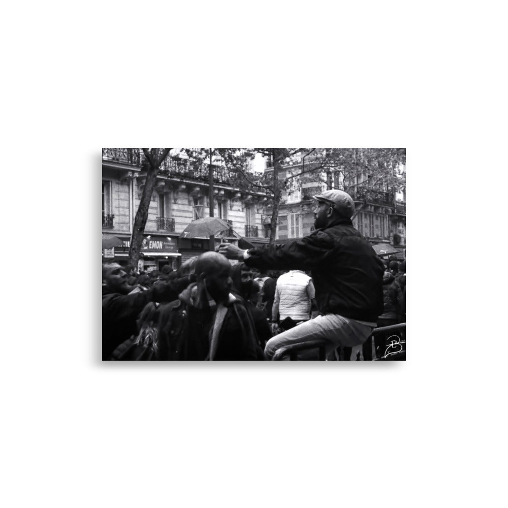 Photographie en noir et blanc capturant un moment intime entre deux manifestants partageant une cigarette durant la Journée internationale des Travailleurs à Paris, œuvre d'Eli Bernet en technique argentique.