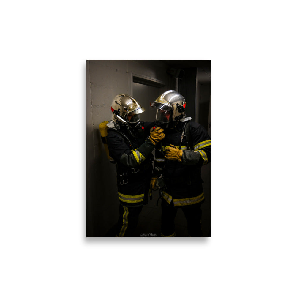 Photographie de deux pompiers en action, s'entraidant lors d'une intervention.