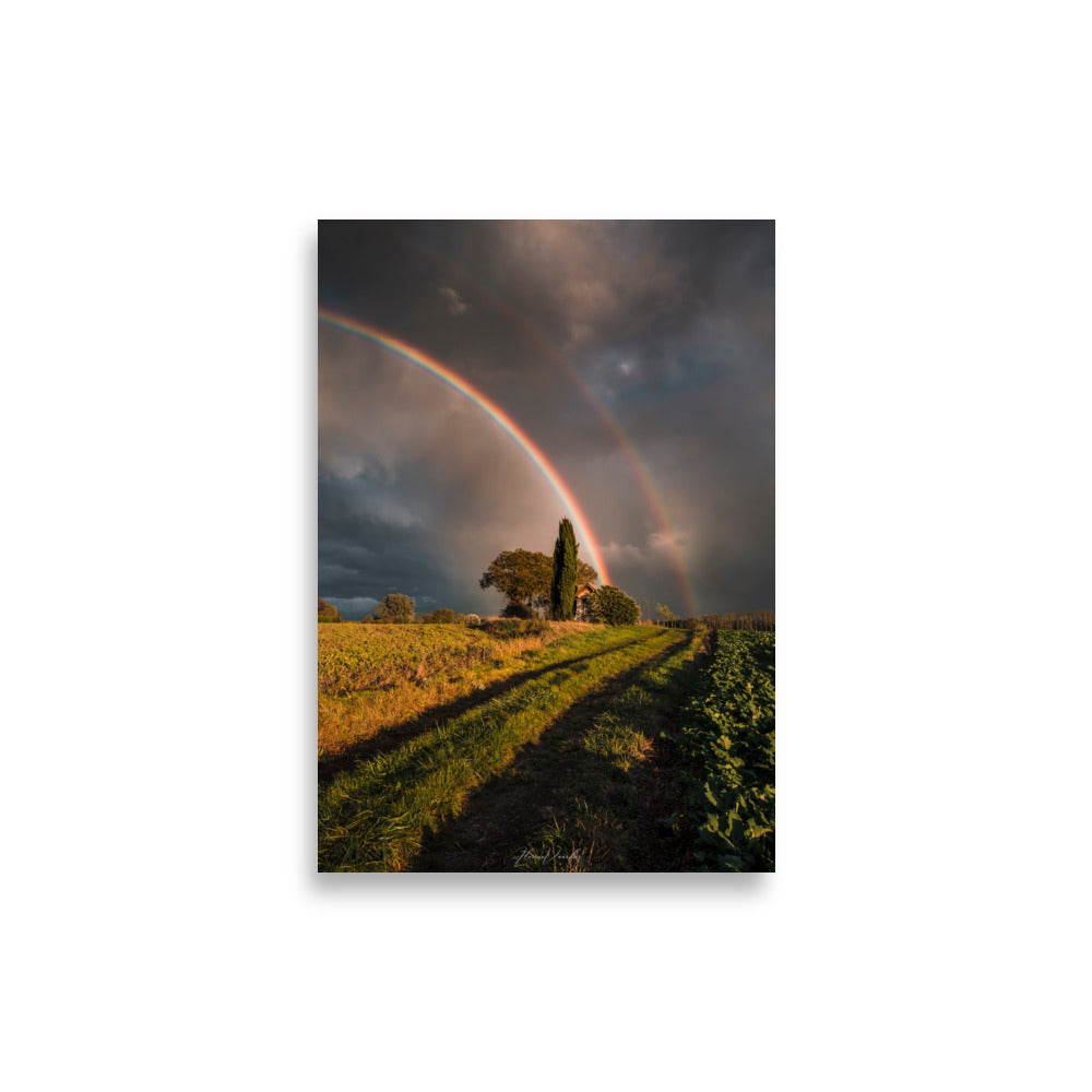 Photographie d'un paysage rural avec un double arc-en-ciel au-dessus d'une maison de campagne, capturée par Florian Vaucher, symbolisant un monde magique et plein d'espoir.