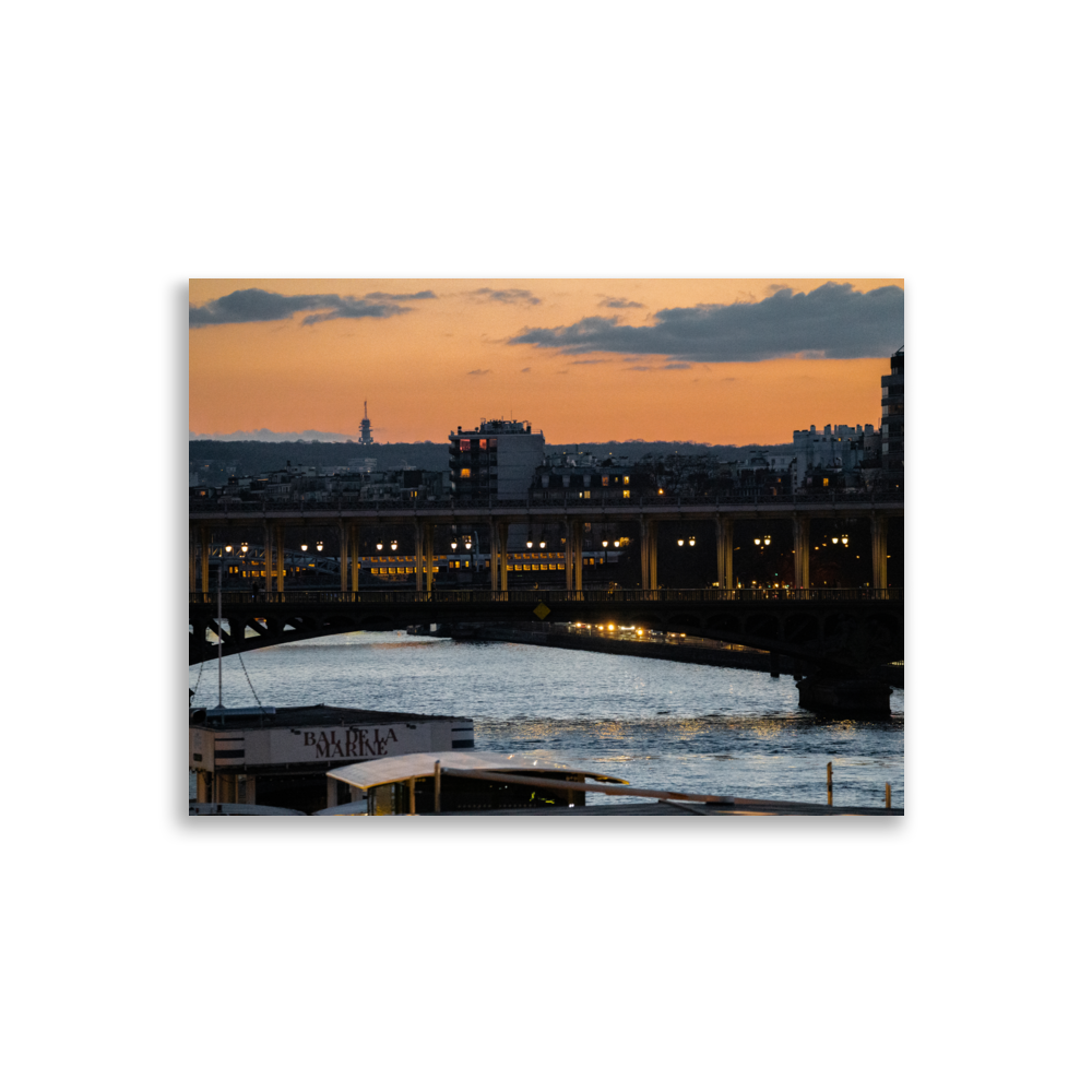 Photographie nocturne du Pont de Bir-Hakeim à Paris, avec des bateaux amarrés aux quais de la Seine et le RER en arrière-plan, sous un ciel teinté d'orange.