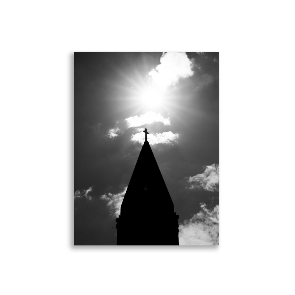 Photographie en noir et blanc du sommet d'une église avec une croix illuminée par le soleil.