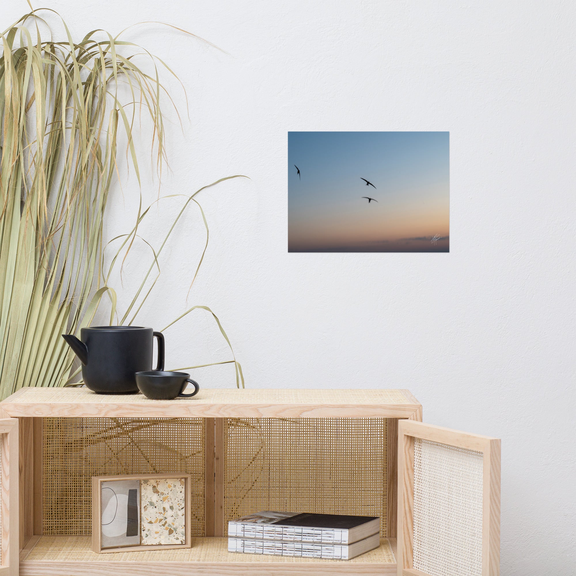 Trois oiseaux volant dans un ciel aux teintes de bleu, orange et jaune.