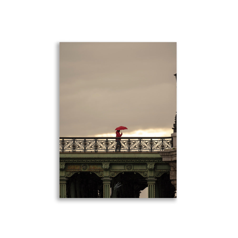 Photographie d'une femme traversant un pont parisien avec un parapluie rouge vif sur fond de paysage pluvieux.