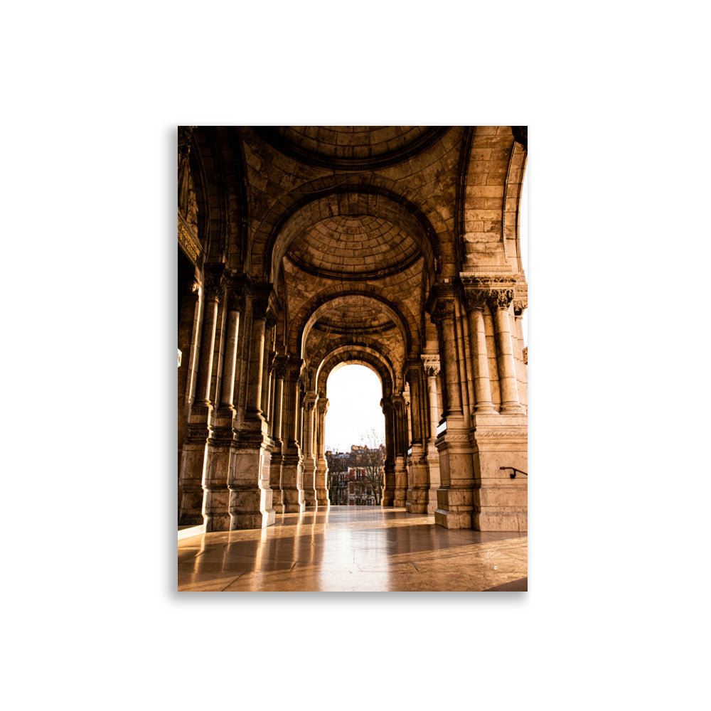 Photographie ensoleillée de la façade de l'entrée de la Basilique du Sacré Cœur à Montmartre, montrant l'architecture détaillée avec des reflets lumineux sur le sol pavé.