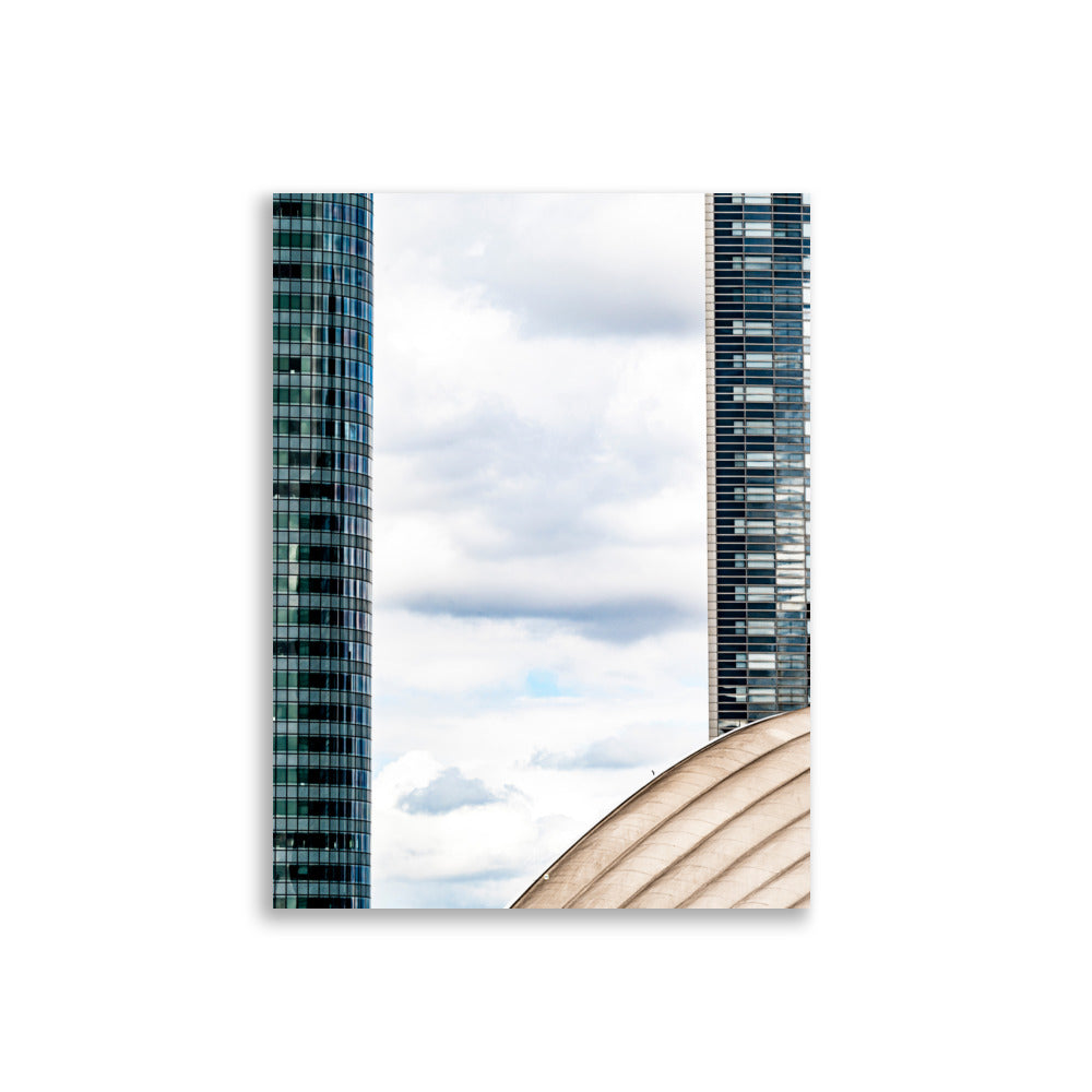 Fenêtre entre deux bâtiments en verre offrant une vue sur un ciel nuageux.