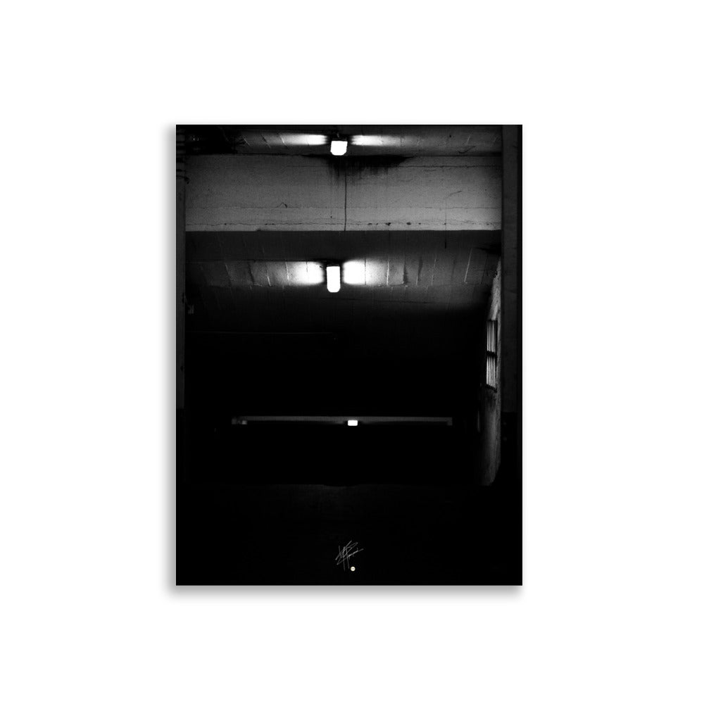 Photographie en noir et blanc intitulée 'Glaçant', montrant trois néons blancs éclairant une entrée de garage descendante dans une atmosphère sombre et mystérieuse.