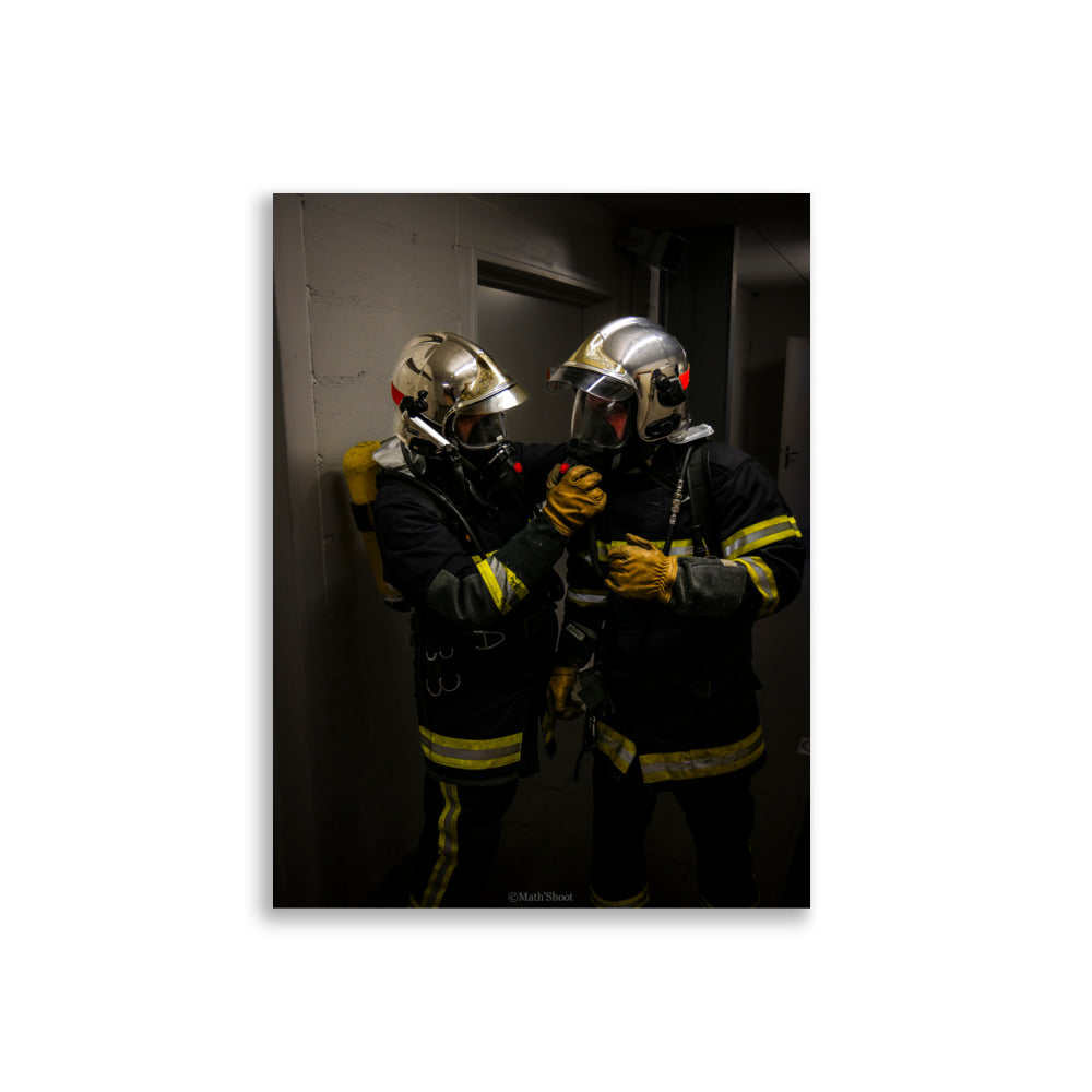 Photographie de deux pompiers en action, s'entraidant lors d'une intervention.