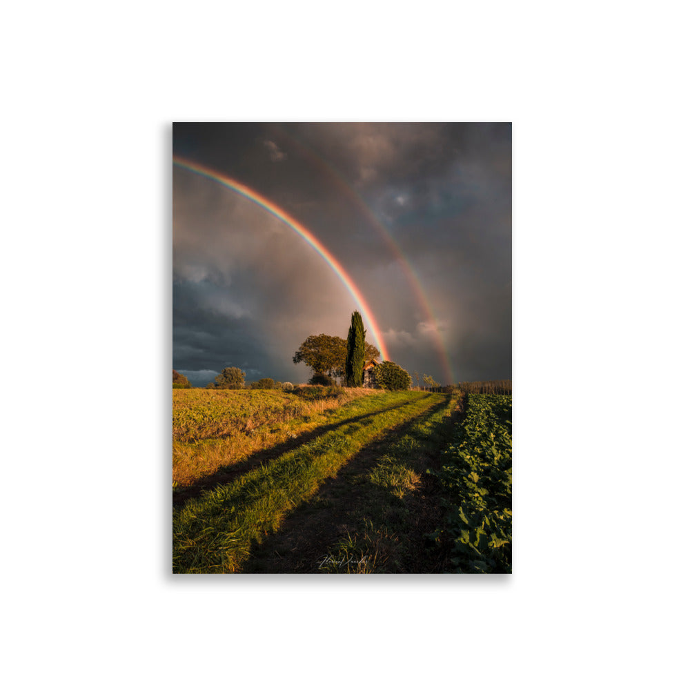 Photographie d'un paysage rural avec un double arc-en-ciel au-dessus d'une maison de campagne, capturée par Florian Vaucher, symbolisant un monde magique et plein d'espoir.