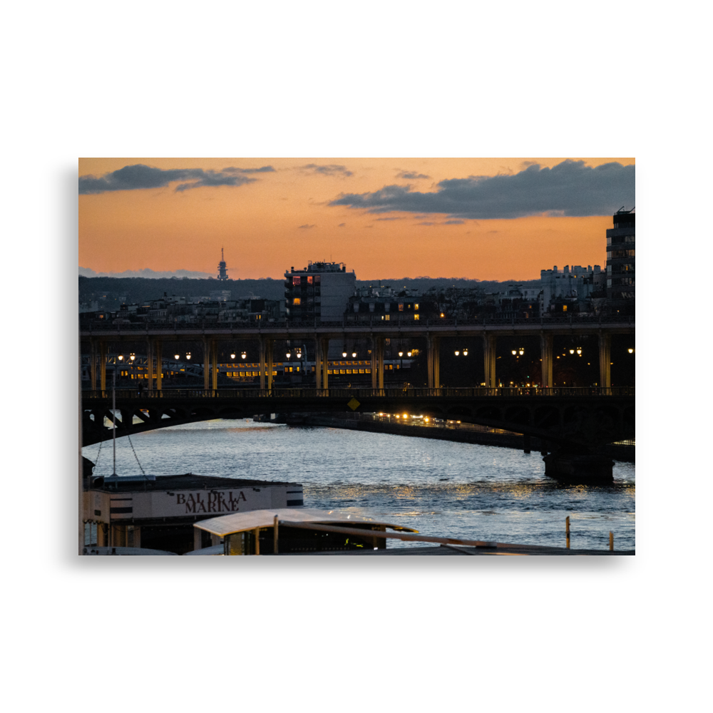Photographie nocturne du Pont de Bir-Hakeim à Paris, avec des bateaux amarrés aux quais de la Seine et le RER en arrière-plan, sous un ciel teinté d'orange.