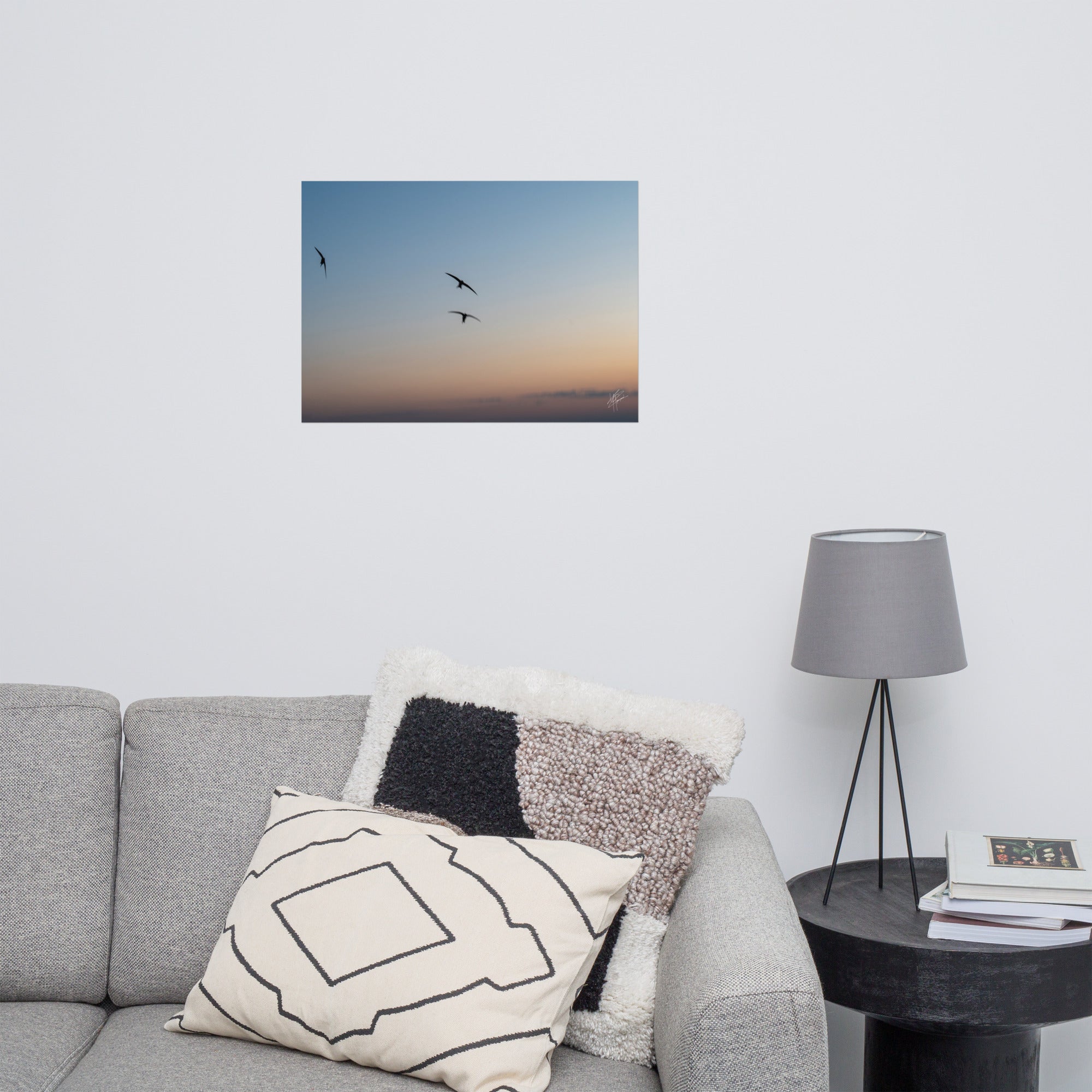 Trois oiseaux volant dans un ciel aux teintes de bleu, orange et jaune.