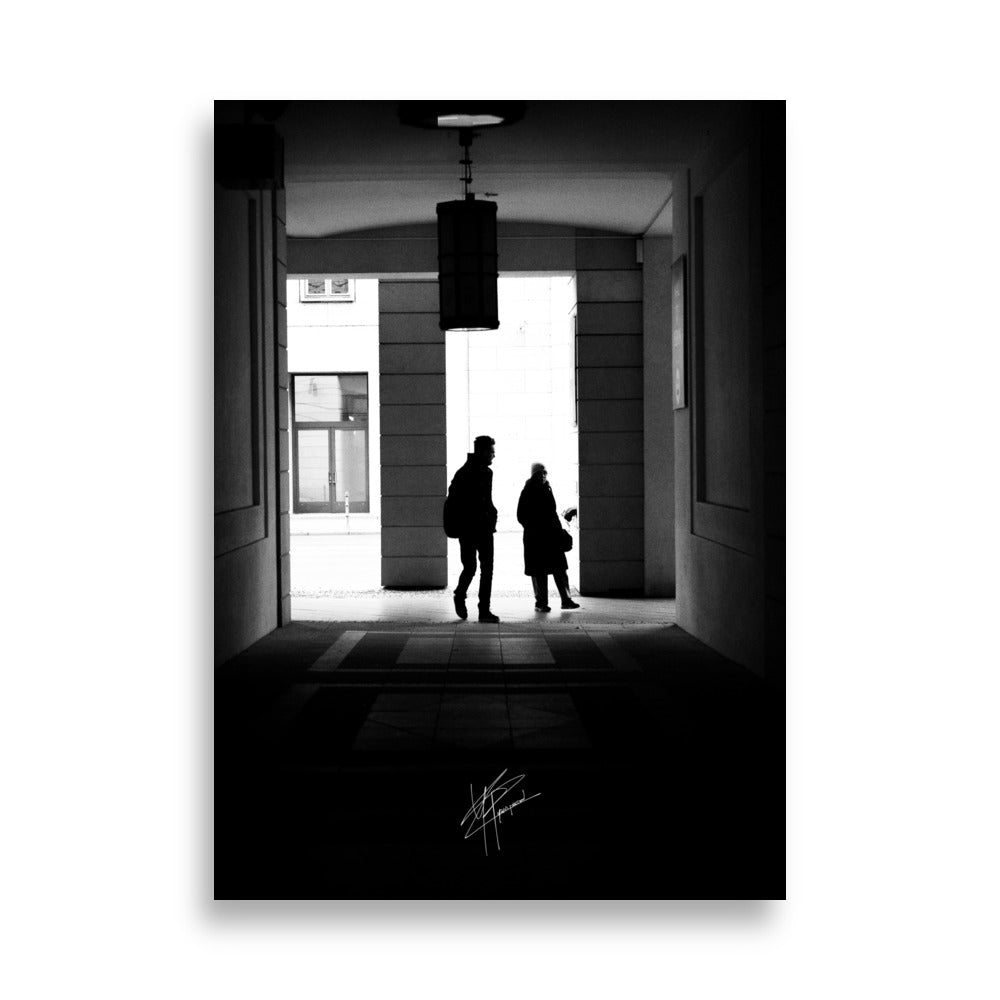 Une allée de Berlin en noir et blanc avec un couple marchant vers une lumière douce.