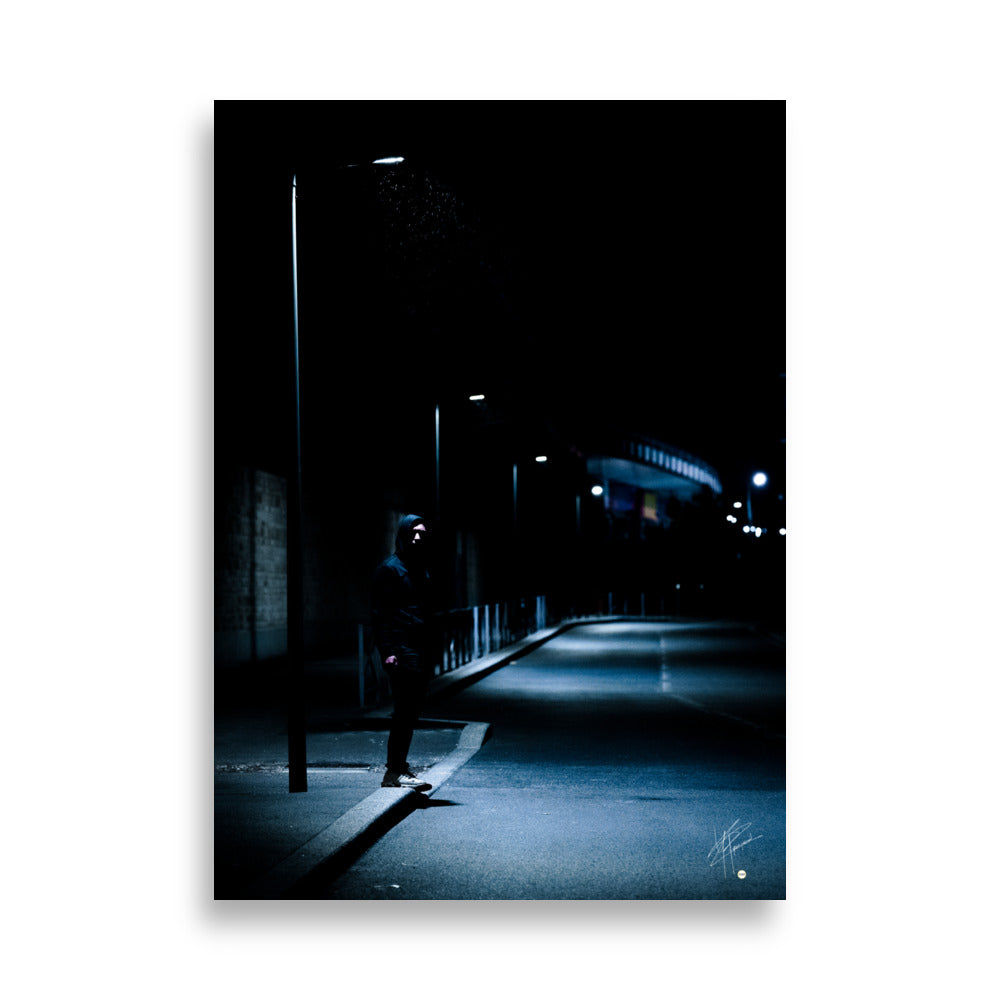 Photographie nocturne d'un homme à capuche se tenant sous un lampadaire près d'une station de métro à Créteil, émanant une atmosphère sombre et énigmatique.