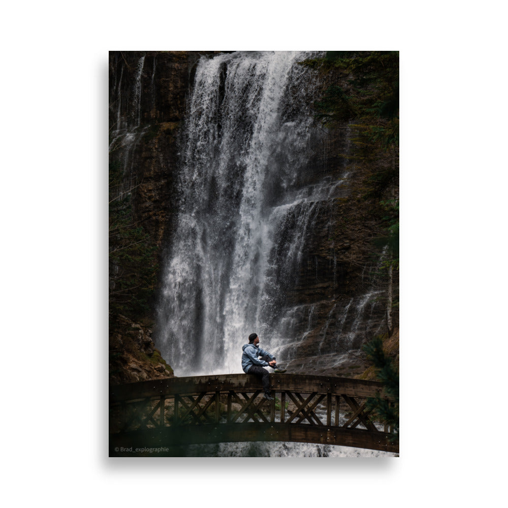 Homme méditatif assis sur une structure en bois au-dessus d'une rivière tumultueuse avec une cascade puissante en arrière-plan – photographie signée par Brad_explographie.