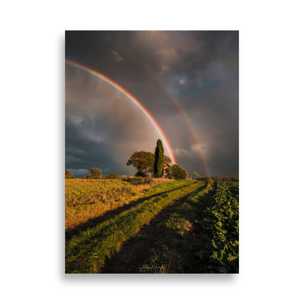 Photographie d'un paysage rural avec un double arc-en-ciel au-dessus d'une maison de campagne, capturée par Florian Vaucher, symbolisant un monde magique et plein d'espoir.