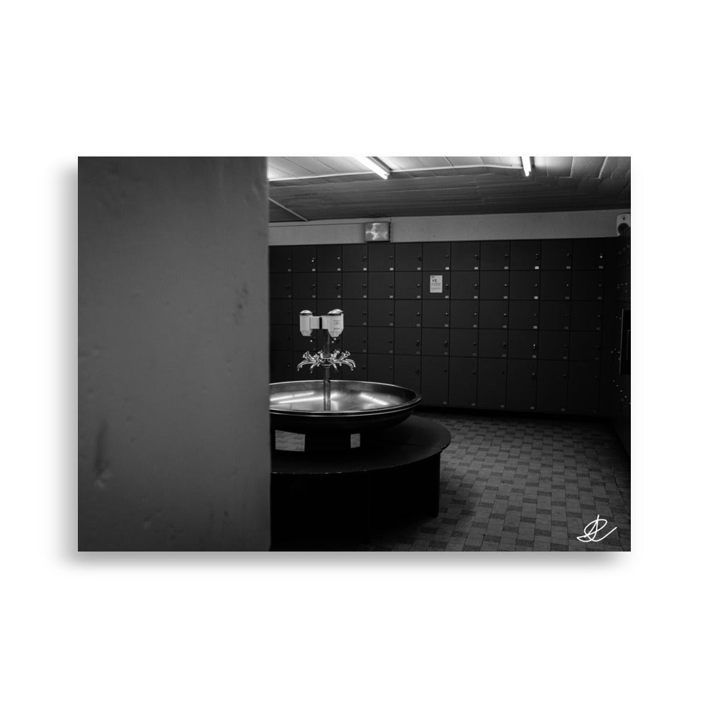 Photographie en noir et blanc d'un vestiaire vide, capturée par Ilan Shoham, offrant une vue discrète et intime, avec une vasque ronde et plusieurs robinets au centre.