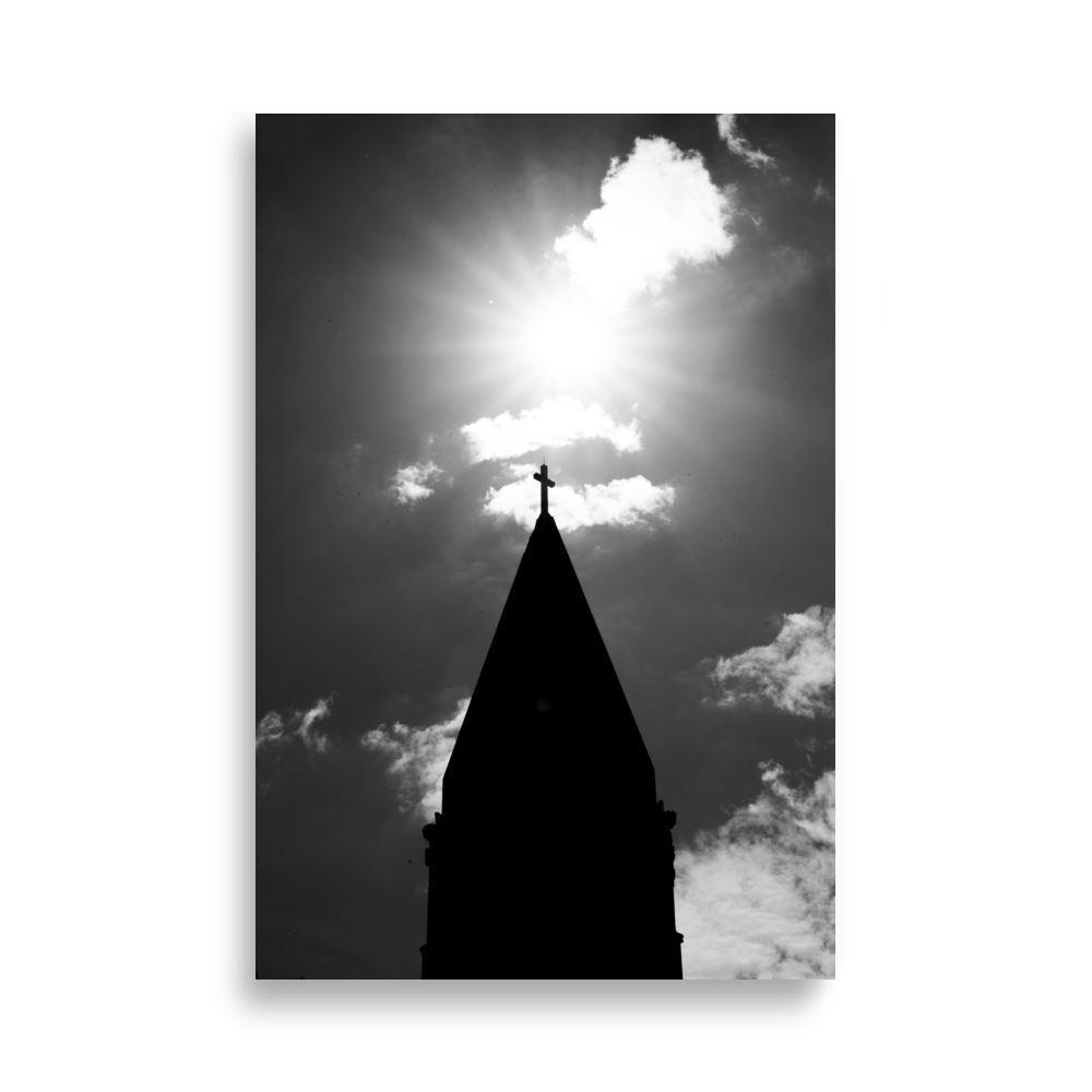 Photographie en noir et blanc du sommet d'une église avec une croix illuminée par le soleil.