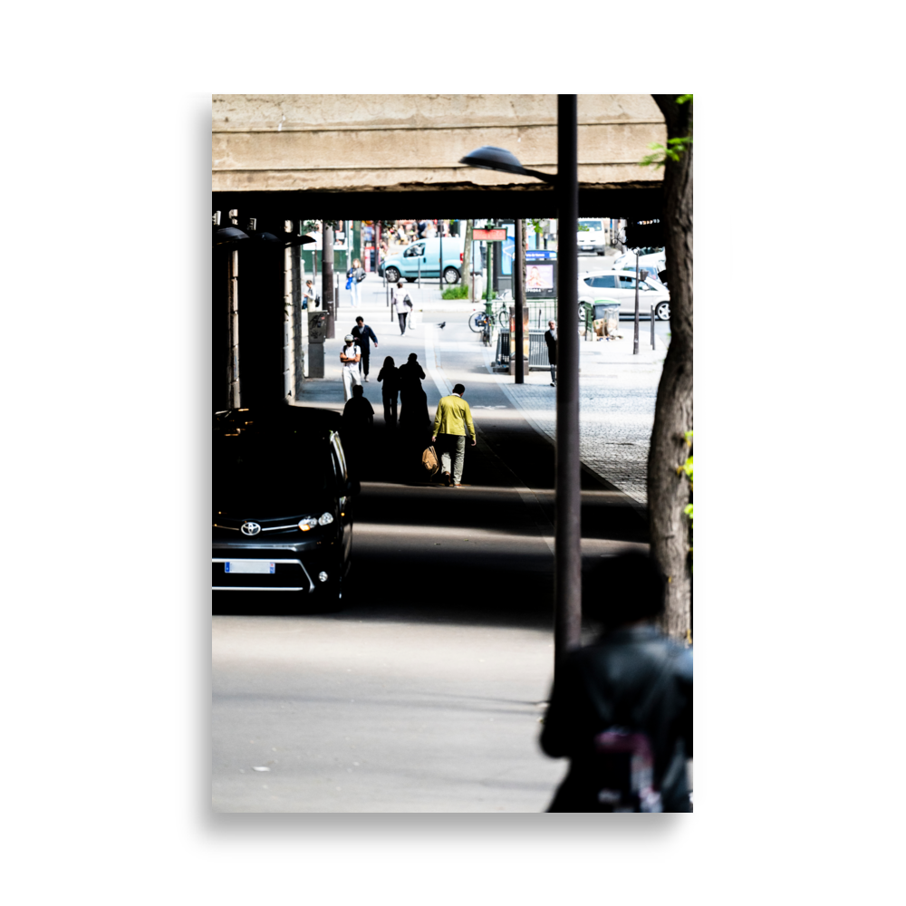 Un homme en veste verte kaki sous un pont ensoleillé.