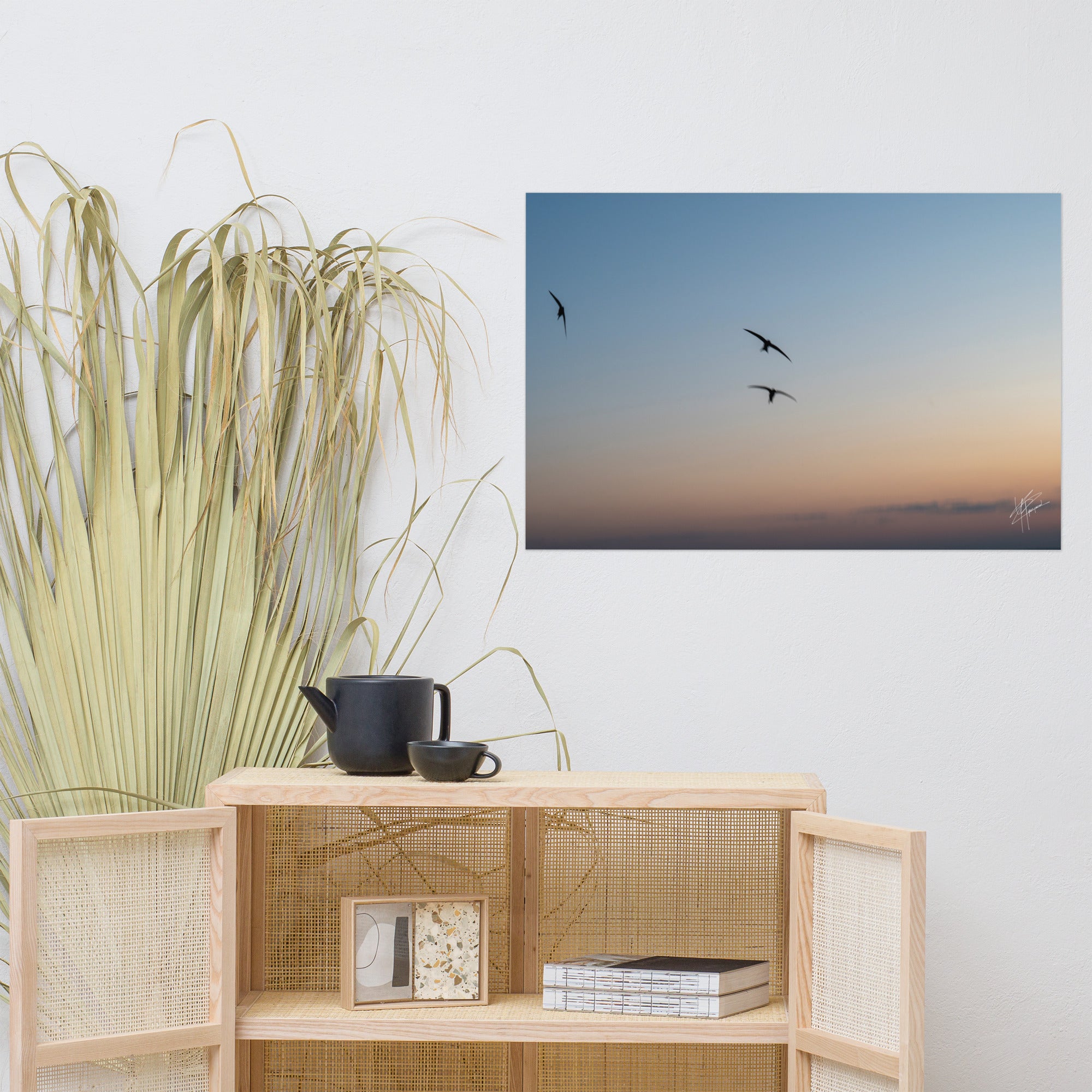 Trois oiseaux volant dans un ciel aux teintes de bleu, orange et jaune.